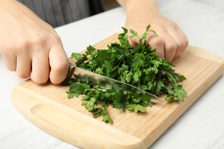Woman cutting fresh green parsley on wooden board at table, closeupの写真素材