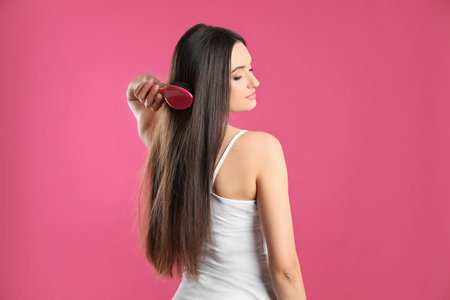 Beautiful young woman with hair brush on color backgroundの写真素材