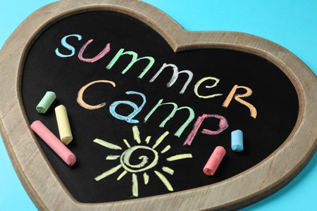 Heart shaped blackboard with text SUMMER CAMP, drawing and chalk sticks on color backgroundの写真素材