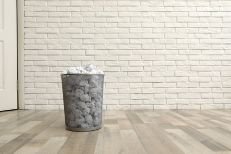 Metal bin with crumpled paper on floor against brick wall, space for textの写真素材