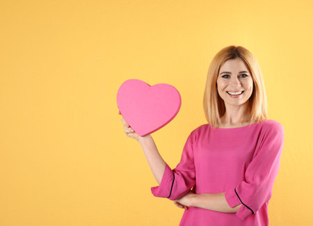 Beautiful woman with heart shaped box on color background. Space for textの写真素材