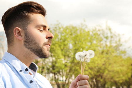 Healthy young man blowing on dandelions outdoors. Allergy free conceptの写真素材