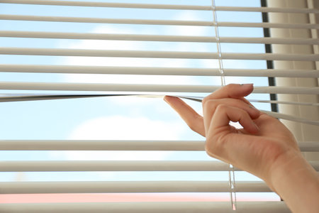 Woman opening horizontal window blinds at home, closeup. Space for textの写真素材