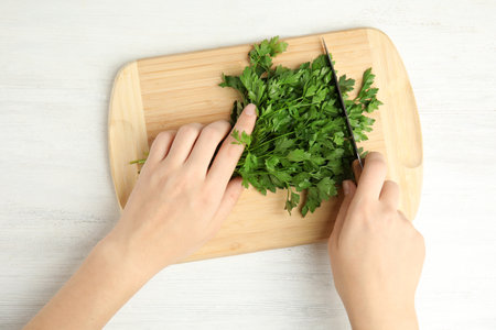 Woman cutting fresh green parsley on wooden board at table, top viewの写真素材