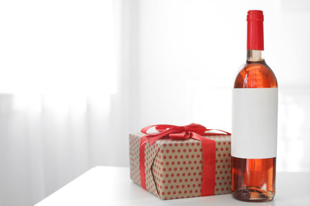 Bottle of wine and gift box on table in light room. Space for textの写真素材