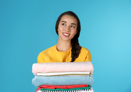 Happy young woman holding clean laundry on color backgroundの写真素材