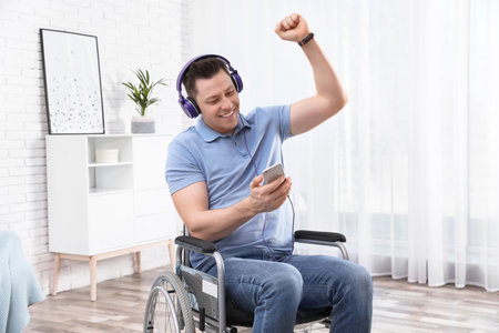 Happy man with headphones and mobile device in wheelchair at home