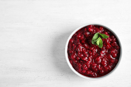 Bowl of tasty cranberry sauce with sauce on white wooden background, top view. Space for textの写真素材