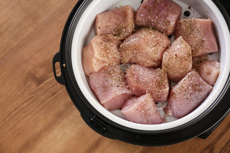 Delicious fresh chicken with spices in modern multi cooker on wooden table, top view. Space for textの写真素材