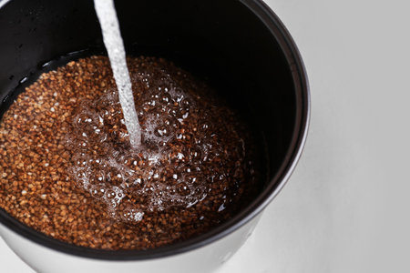 Pouring water into multi cooker with buckwheat on light background, closeupの写真素材