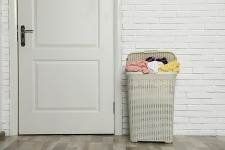 Plastic laundry basket full of dirty clothes near brick wall in room. Space for textの写真素材