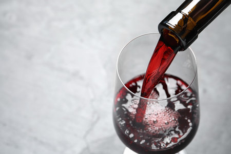 Pouring red wine from bottle into glass on light background, closeup. Space for textの写真素材