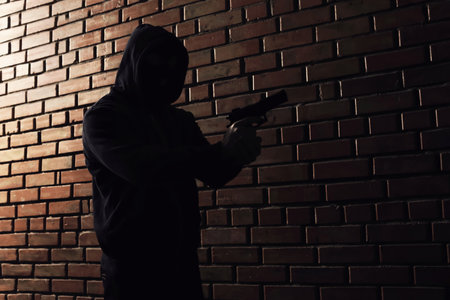 Man in hoodie with gun indoors. Dangerous criminalの写真素材