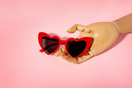 Wooden mannequin hand with stylish heart shaped glasses on color backgroundの写真素材