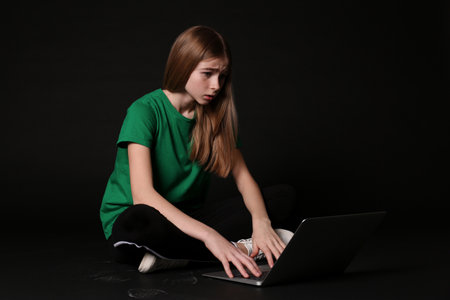 Shocked teenager girl with laptop on black background. Danger of internet