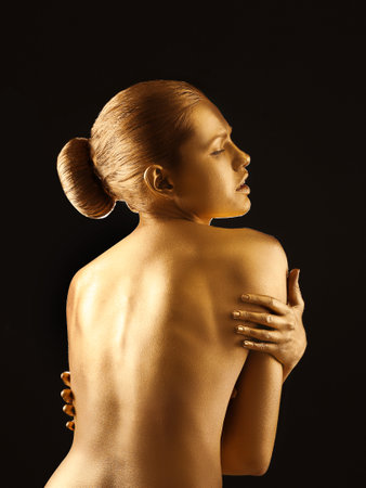 Portrait of beautiful lady with gold paint on skin against black backgroundの写真素材