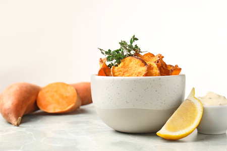 Bowl of sweet potato chips with sauce and lemon on table against white background. Space for textの写真素材
