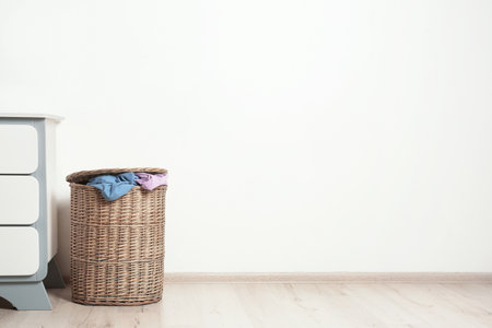 Wicker laundry basket with dirty clothes on floor near wall. Space for textの写真素材