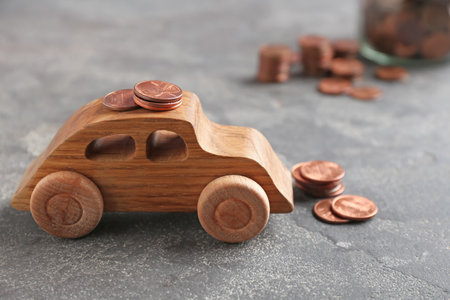 Wooden car model and coins on gray backgroundの写真素材