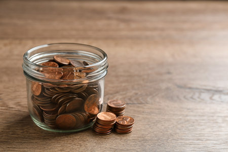 Glass jar with coins on wooden table, space for text. money saving concept