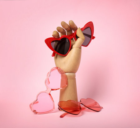 Wooden mannequin hand with stylish heart shaped glasses on color backgroundの写真素材