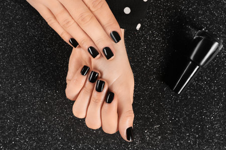 Woman with black manicure and nail polish bottle on dark background, top viewの写真素材