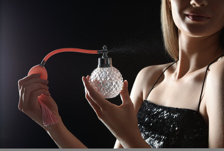Young woman applying perfume against black background, closeupの写真素材