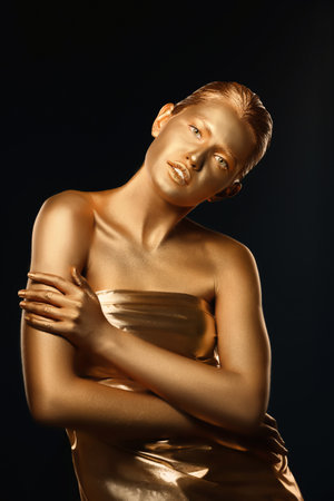 Portrait of beautiful lady with gold paint on skin against black backgroundの写真素材