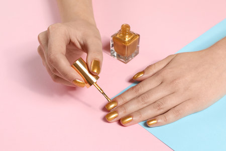 Woman painting nails with golden polish on color background, closeupの写真素材