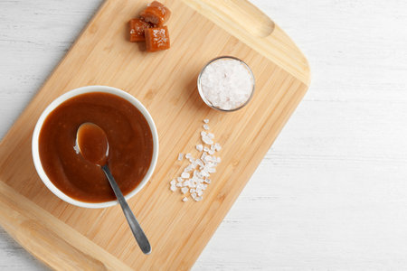 Flat lay composition with bowl of caramel sauce and salt on wooden table. Space for textの写真素材