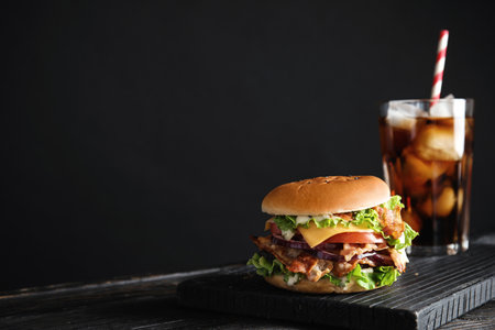 Tasty burger with bacon and cola on black background. Space for textの写真素材