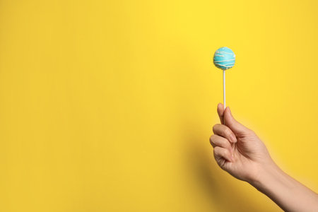 Woman holding bright delicious cake pop on color background, closeup. Space for textの写真素材