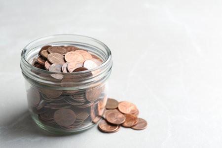Glass jar and coins on light background. Space for textの写真素材