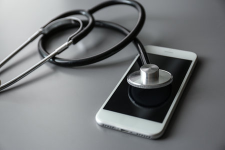 Smartphone and stethoscope on gray table, closeup with space for text. Repair serviceの写真素材
