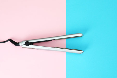 Modern hair iron for straightening on color background, top view