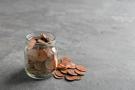 Glass jar and coins on gray table. Space for text