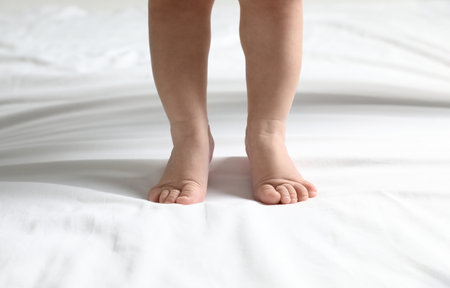 Cute little baby standing on white bed sheet, closeupの写真素材