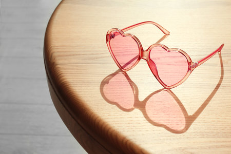 Stylish heart shaped sunglasses on wooden table. Space for textの写真素材