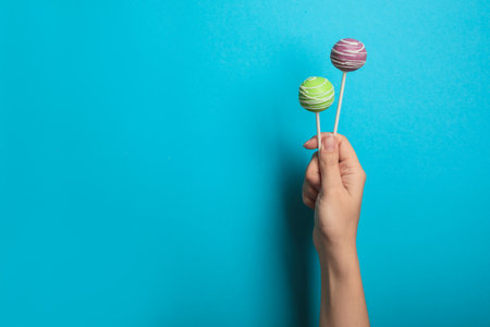 Woman holding bright delicious cake pops on color background, closeup. Space for textの写真素材