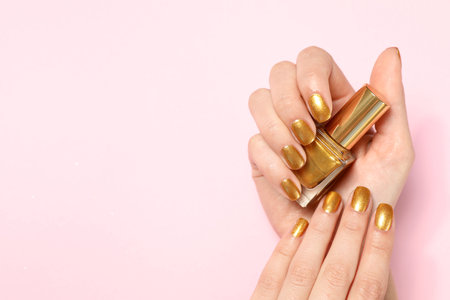 Woman holding bottle of golden nail polish in manicured hand on color background, top view. Space for textの写真素材