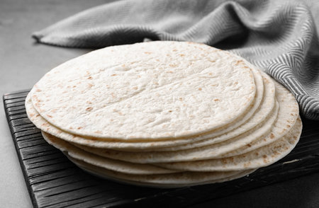 Wooden board with corn tortillas on table, closeup. Unleavened bread