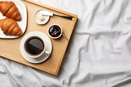 Top view of wooden tray with coffee, croissants, butter and jam on white fabric, space for text. breakfast in bedの写真素材