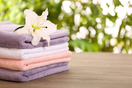 Stack of clean towels with lily on table against blurred background. Space for textの写真素材