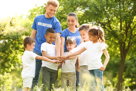 Group of kids joining hands with volunteers in the parkの写真素材