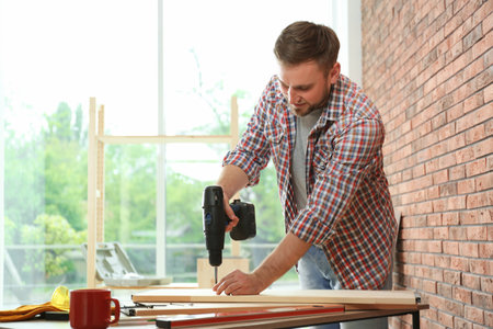 Young man working with electric screwdriver near brick wall. Space for textの写真素材