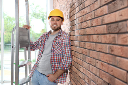 Young working man with ladder near brick wall. Space for textの写真素材