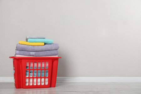 Laundry basket with clean towels on floor near light wall. Space for textの写真素材