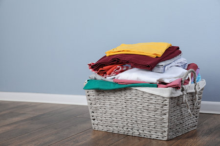 Wicker laundry basket with clean clothes on floor near color wall. Space for textの写真素材