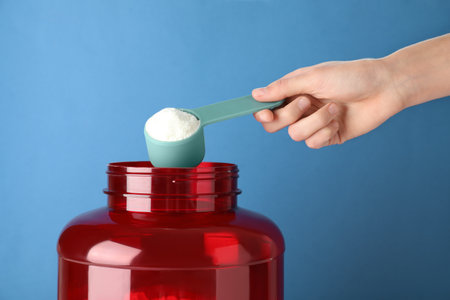 Man taking protein powder with scoop from jar against color background, closeupの写真素材