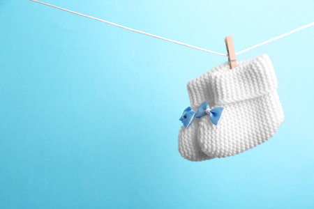 Knitted booties hanging on washing line against color background, space for text. baby accessories